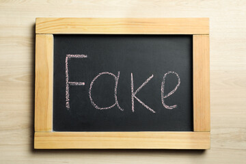 Obraz premium Board with word FAKE on wooden table, top view