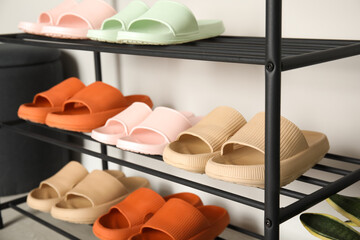 Shoe rack with different pairs of rubber slippers near white wall indoors, closeup