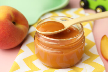 Spoon with healthy baby food over glass jar on pink wooden table, closeup