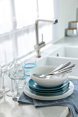 Different clean dishware, cutlery and glasses on countertop in kitchen