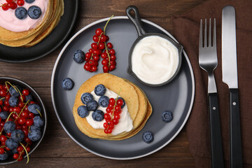 Fototapeta na wymiar Tasty pancakes with natural yogurt, blueberries and red currants on wooden table, flat lay