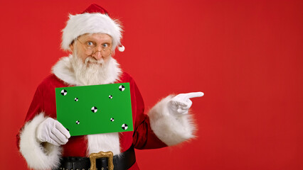 Cheerful Santa Claus Holding Green Screen Banner Tracking Points for Copy Space. Blank Green Screen Board. Shows an Approving Thumbs-up Gesture With Space for Text or Advertising on Red Background. - Powered by Adobe