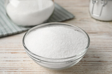 Fototapeta na wymiar Granulated sugar in glass bowl on white wooden table, closeup