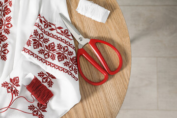 White shirt with beautiful embroidery design, threads and scissors on wooden table, flat lay....