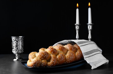 Homemade braided bread with sesame seeds, goblet and candles on dark grey table. Traditional...
