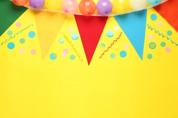 Bunting with colorful triangular flags and other festive decor on yellow background, flat lay. Space for text