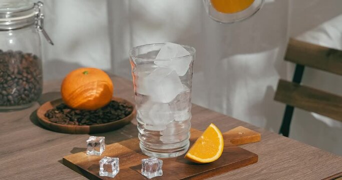 4k video, Healthy iced orange drink poured in glass. used hand pouring fruit juice into cup with iced. Some might drink orange refreshing infused water with gin for cocktail. cold beverage summer