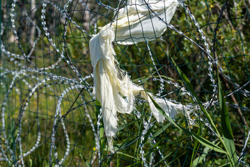 Fence with razor wire in sunny day. A piece of cloth remained caught in the fence. Selective focus.