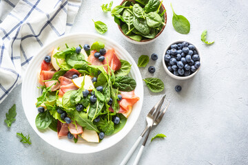 Healthy salad with spinach, arugula, jamon, pear, blueberry and parmesan. Top view on white background.