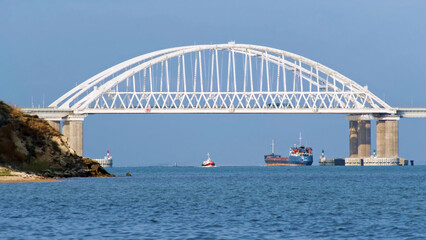 Fototapeta na wymiar Breathtaking seascape with a white beautiful bridge with many moving cars above the water surface and sailing ships, time lapse effect. Shot. Calm sea with ripples, huge bridge, vessel and bue sky.
