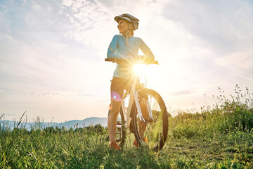 Cyclist Woman riding bike in helmets go in sports outdoors on sunny day a mountain in the forest. Silhouette female at sunset. Fresh air. Health care, authenticity, sense of balance and calmness.
 - obrazy, fototapety, plakaty