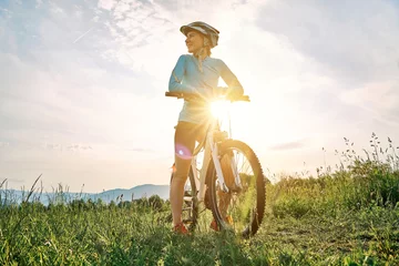 Foto op Plexiglas Cyclist Woman riding bike in helmets go in sports outdoors on sunny day a mountain in the forest. Silhouette female at sunset. Fresh air. Health care, authenticity, sense of balance and calmness.  © Andrii IURLOV