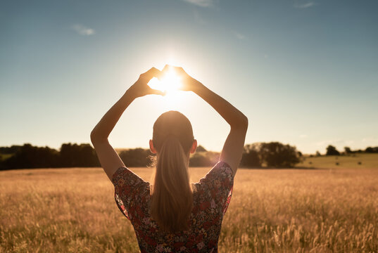 I love nature. Woman making a hand heart shape in field at sunset. 