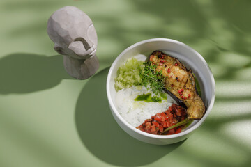 baked eggplant with white sauce and lettuce on green background with shadow from palm tree, top view