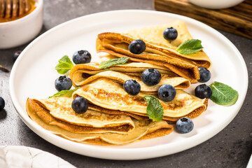 Crepes with blueberries and honey at kitchen table. Healthy breakfast or snack.