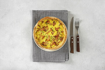 Homemade quiche with chanterelle mushrooms served on gray napkin on light background, top view, copy space