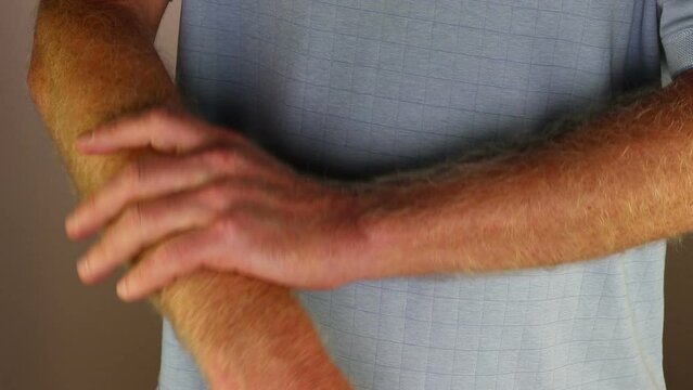 Close-up of right forearm self massaging with left hand by an adult caucasian male wearing a blue shirt. White mature guy massaging his right forearm arm with his left hand close-up indoors