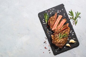 Grilled beef steak striploin medium rare on slate serving board at light stone table. Top view with...