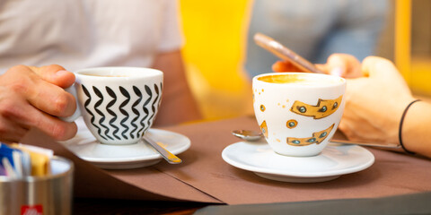 A couple are seated at a table with two cups of coffee outside an Italian restaurant