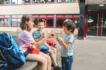 Children sit on a bench in the school yard and eat apples and sandwiches. Snack during break time during class