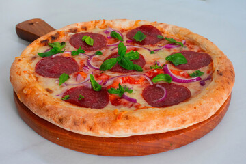 Delicious homemade pepperoni pizza with a thick crust on a wooden board with basil and red onions on a white marble kitchen top 