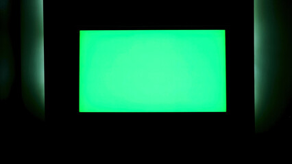 TV with horizontal green screen on a black wall with green illumination. Concept. Close up of chroma key TV screen in a dark room at night.