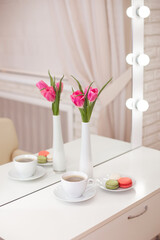 
Client's place in hairdressing and beauty salon with cup of coffee, macaroons and pink tulips in vase. 