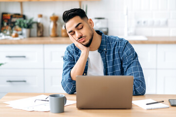 Tired overworked arabian or indian young male, company worker, student, working remotely at home...