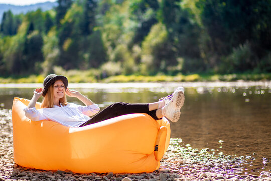 Summer lifestyle portrait of pretty smiling girl lying on yellow inflatable sofa outdoor on river bank. Relaxing, enjoying life on air bed. Beach vacation woman happy lying at holiday resort. Girl
