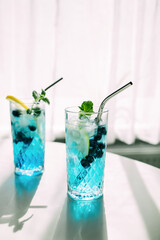 Summer bright blue curacao drink decorated with a slice of lemon and mint on a table opposite the window. Refreshing cocktails with fresh berries