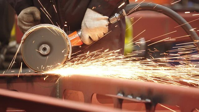 Close-up of metalwork processing at train car production plant. sparks fly. factory worker hands in protective uniform, holding the metalworking tool.