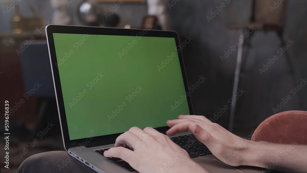 Poster over the shoulder view of a man sitting at his desk and working on a laptop with green screen. stock