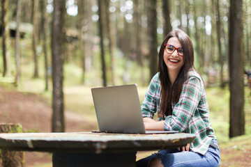 Young latin woman sitting in the forest working with laptop freelancing looking camera smiling at Costa Rica