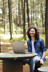 Young latin man sitting in the forest working with lapto looking camera smiling at Costa Rica