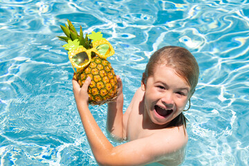 Child in swimming pool playing in summer water. Vacation and traveling with kids. Cute little boy swim on watter pool in the summer. Kids beach fun. Funny pineapple fruit for children.