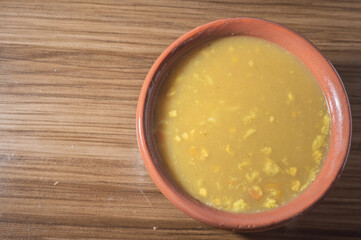 Yellow soup in a clay bowl,the soup is on a wooden table with copy space and spoon