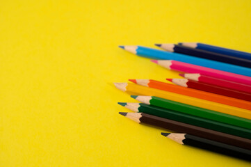 A row of unevenly arranged colored pencils on a yellow background with copy space.