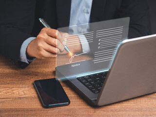 Electronic signature. A businessman in a suit uses a pen to sign electronic documents on digital...