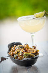 Charred Brussels Sprouts Drizzled with Aioli in a cast iron dish accompanied by a cocktail.