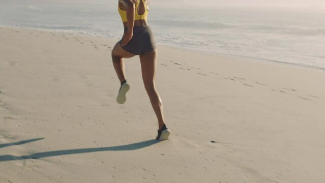 Active athlete legs keeping fit, running on the beach front of ocean or sandy seaside. Female jogger doing morning workout and exercise for a healthy lifestyle. Back view of sporty woman training.
