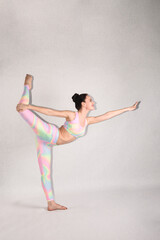 Fototapeta na wymiar A beautiful slender gymnast in a tracksuit does sports or yoga in the studio in the swan pose
