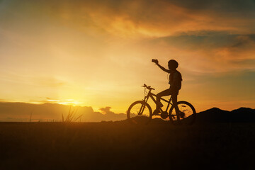 Fototapeta na wymiar Silhouette of woman riding bicycle at sunset, cheerfully at the end of the day. Woman riding break relax and take a photo landscape and looking forward with beautiful nature at sunset time.