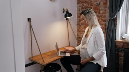 Pregnancy and work concept. Middle-aged caucasian pregnant businesswoman working on a new project while sitting at her office desk with a laptop. Formal wear. Maternity wear. High quality 4k footage - Powered by Adobe