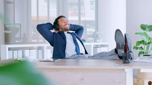 Successful entrepreneur listening to music while feeling satisfied and relieved once done completing deadlines in an office. Young business man enjoying a break to rest with a podcast with headphones
