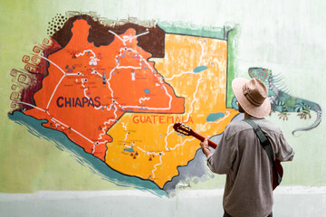 An unrecognizable young musician is watching a Chiapas map painted on a wall thinking where to go