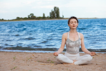 Fototapeta na wymiar Woman practicing yoga outside in lotus pose on beach