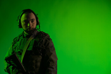 soldier in the studio on a green background with colored light. a man in military uniform with a gun, rifle or machine gun. military. airball player