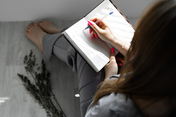 young woman in a gray satin trendy pantsuit with herbs and a notebook. beautiful stylish photo in minimalism on the floor. white studio. herbs. the beauty. beauty, fashion concept