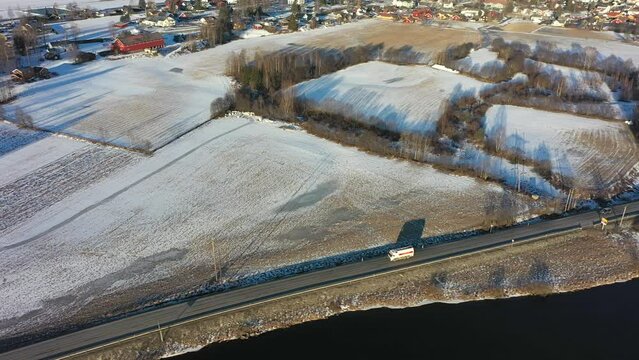 Truck and car driving along highway during morning sunrise with long shadows in Nesbyen Norway - Beautiful aerial with cars in front and frosty farmland in background