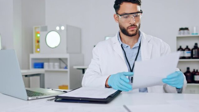 A serious male scientist looking at medical data in a laboratory. A science researcher doing research for a scientific journal. Intelligent lab worker working on a covid cure